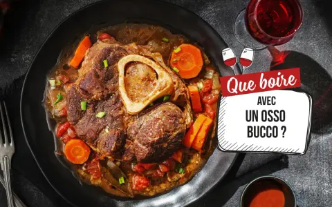 Un plat d'osso bucco savoureux, avec carottes et tomates, servi sur une assiette noire. La question "Quel vin avec osso bucco ?" est mise en avant.