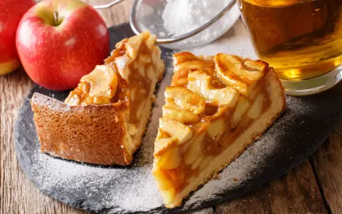 Deux parts de tarte aux pommes, saupoudrées de sucre glace, avec des pommes fraîches et un verre de cidre. Une belle idée de que faire avec des pommes.