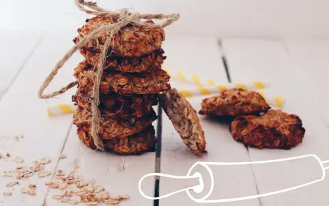 Pile de cookies healthy flocons d'avoine, liés par une cordelette. Quelques flocons éparpillés et des pailles rayées en arrière-plan.