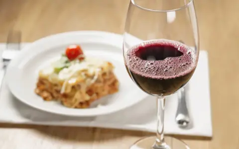 Un verre de vin rouge pétillant à côté d'une portion de lasagnes appétissante. La question se pose : quel vin avec des lasagnes pour un accord parfait ?
