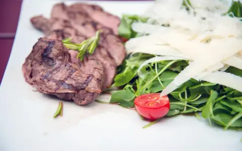 Délicieuse tagliata de boeuf grillée, servie avec une salade verte, copeaux de parmesan et une moitié de tomate cerise.