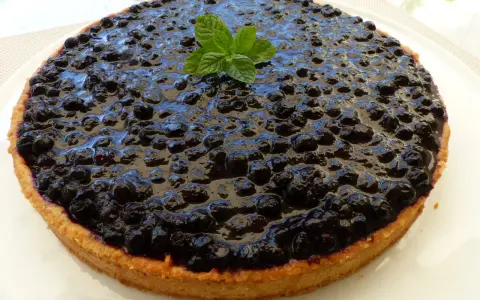 Tarte myrtille amande, une gourmandise aux myrtilles juteuses et à la pâte sablée aux amandes, décorée d'une touche de menthe fraîche.