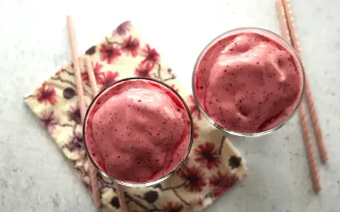 Deux verres remplis d'un onctueux milkshake fruit rouge, accompagnés de pailles roses et d'une serviette fleurie.
