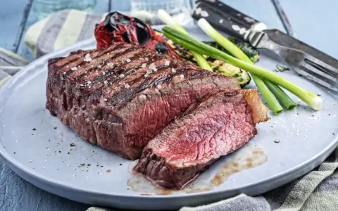 Un savoureux rumsteck de boeuf grillé, coupé en tranches, servi avec des légumes rôtis et des oignons verts sur une assiette grise.