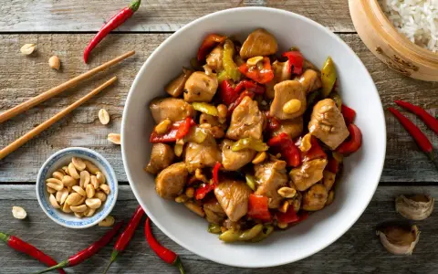 Un délicieux poulet kung pao, garni de cacahuètes croquantes, de poivrons rouges et verts, prêt à être dégusté avec des baguettes.