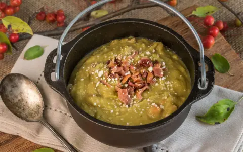 Soupe de pois cassés réconfortante, garnie de lardons croustillants et de fromage râpé, servie dans une cocotte en fonte rustique.