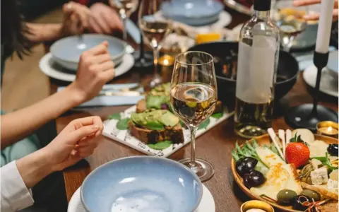 Un verre de vin blanc beurré, des toasts à l'avocat et un plateau de fromages et fruits sur une table dressée pour un dîner convivial.
