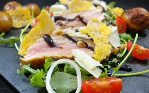 Délicieuse tagliata de veau, servie sur un lit de roquette avec des tomates cerises, des oignons et des tuiles de parmesan croustillantes.