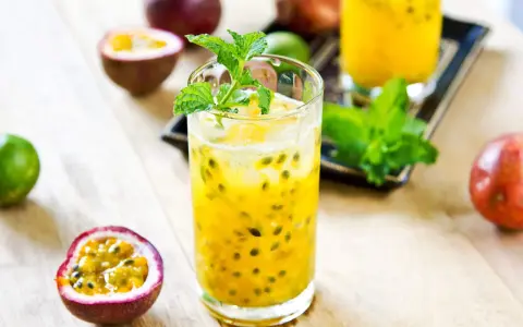 Un verre de cocktail fruit de la passion, garni de menthe fraîche, entouré de fruits entiers et coupés.