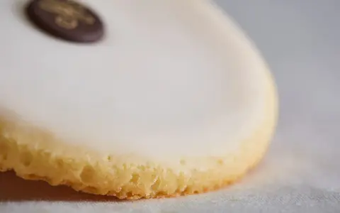 Un palet de dame, biscuit sablé glacé de blanc, orné d'un médaillon chocolat doré.