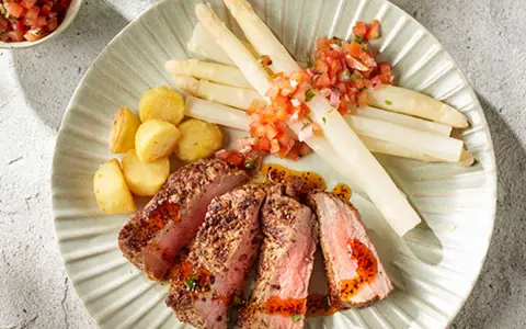 Tranches de viande juteuse avec asperges blanches et pommes de terre sautées, un accompagnement parfait pour un repas savoureux.