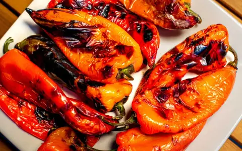 Poivrons rouges et orangés grillés au barbecue, légèrement noircis par la flamme, sur une assiette blanche. Un délice estival.