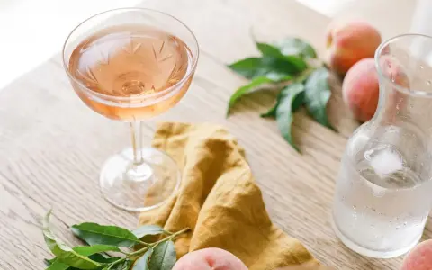 Un verre de vin de pêche rosé, des pêches fraîches et une carafe d'eau glacée sur une table en bois.