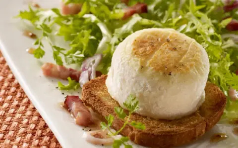 Une délicieuse salade de chèvre chaud sur toast, garnie de lardons et de persil frais, sur une assiette blanche.