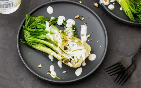 Une assiette de pak choi cru arrosé d'une sauce crémeuse, garni de graines et de zeste de citron vert.