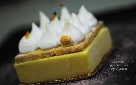 Une tranche de tarte au citron meringuée, avec sa crème jaune pâle, sa fine couche de biscuit et ses pointes de meringue légèrement caramélisées.