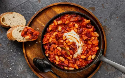 Délicieuse recette baked beans dans une poêle, garnie de crème, servie avec du pain grillé. Un plat réconfortant et savoureux.