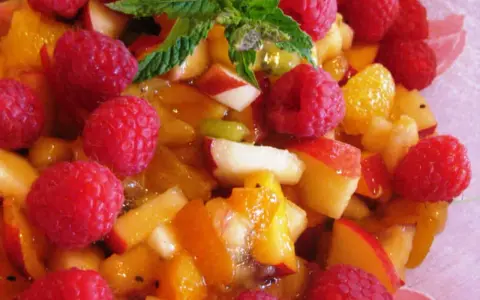 Une délicieuse salade de fruits d'été, pleine de framboises, pêches et abricots juteux, garnie de menthe fraîche.
