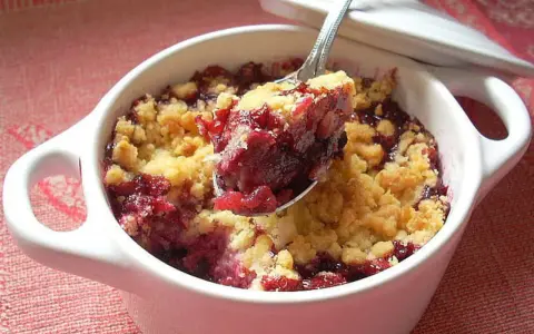 Cuillère de crumble fruits rouges, un délice croustillant et fruité dans un ramequin blanc.