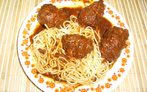 Un plat de spaghetti avec des ragoûts de bœuf en sauce, ressemblant à des alouettes sans tête, sur une assiette décorée de fleurs.