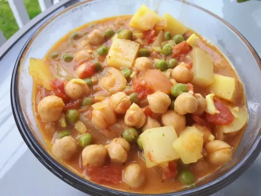 Un savoureux curry de petit pois avec des pois chiches et des morceaux de pommes de terre dans une sauce orangée.