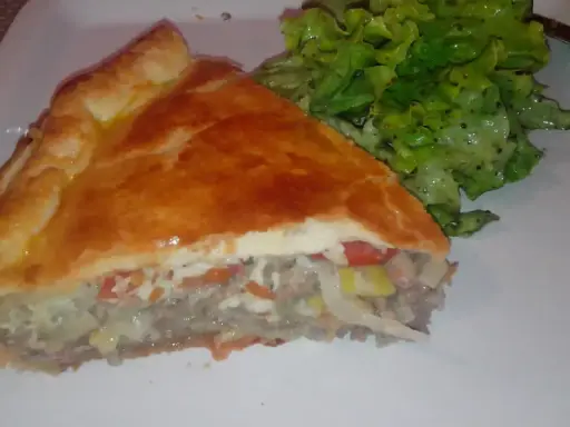 Une part de tourte à la viande grand-mère, dorée et généreuse, servie avec une salade verte croquante. Un délice réconfortant.