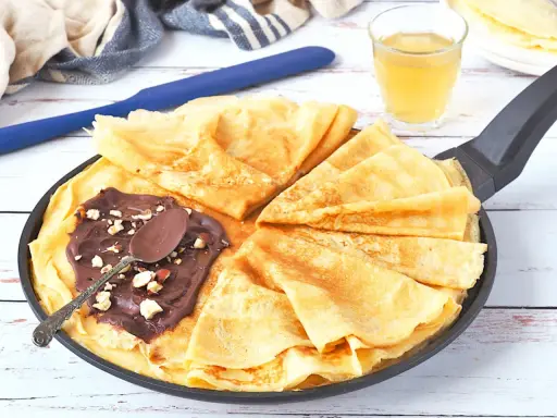 Délicieux crepe a la biere, pliés dans une poêle, garnis de pâte à tartiner au chocolat et noisettes. Une cuillère repose sur le dessus.