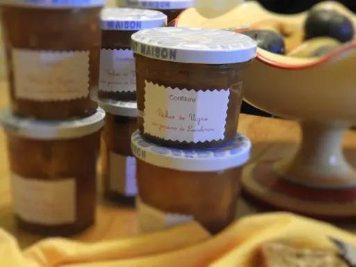 Plusieurs pots de confiture maison, dont une délicieuse confiture de pêches de vignes, sont alignés sur une table en bois.