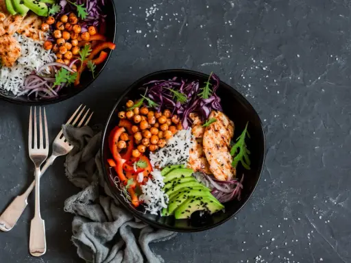 Deux bols de poulet grillé, riz, avocat, pois chiches et chou rouge. Une recette avec salade verte pour un repas sain et coloré.