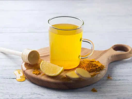 Une tasse de boisson gingembre citron curcuma, avec des tranches de citron, du gingembre frais et du curcuma en poudre.