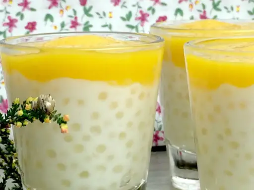 Trois verres de tapioca au lait de coco, surmontés d'une purée jaune, avec une petite branche de bruyère en premier plan.