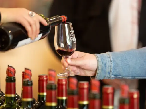 Service d'un vin rouge fruité et doux dans un verre, avec des bouteilles alignées en arrière-plan.