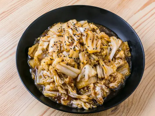 Un plat de recette pak choï sauté, garni de graines de sésame noires et blanches, sur une assiette noire.