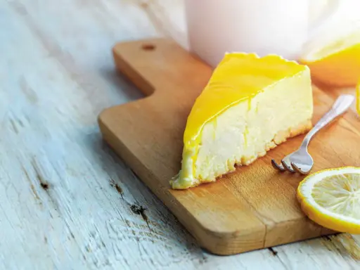 Tranche de cheesecake au citron, une recette Philadelphia sans cuisson, sur une planche en bois avec une fourchette et des rondelles de citron.