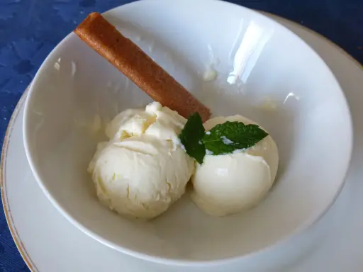 Deux boules de glace au citron onctueuse, garnies de menthe fraîche et d'un biscuit fin, dans un bol blanc.