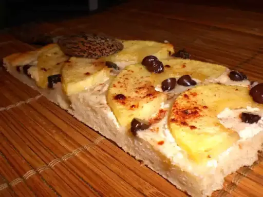 Tranche de tarte flambée sucrée aux pommes, cannelle et pépites de chocolat, posée sur un tapis de bambou.