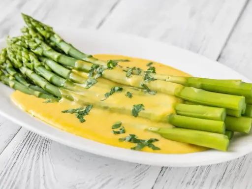 Un bouquet d'asperges vertes nappées d'une sauce hollandaise crémeuse, garnies de persil frais. Une délicieuse idée d'asperges en entrée froide.