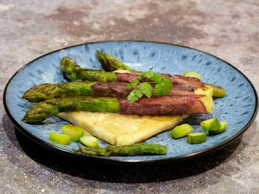 Asperge à la poêle enroulée de viande séchée, servie sur du pain grillé, garnie de persil frais et de morceaux d'asperges.