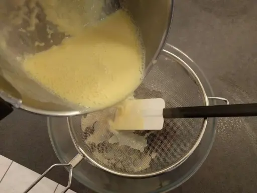 Filtrage de la crème anglaise pour une texture parfaite. Une spatule aide à racler le fond de la casserole.