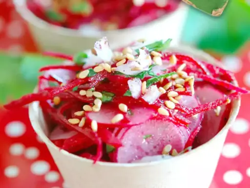 Salade de radis rose râpé et en tranches, garnie de graines de sésame et d'herbes fraîches, servie dans un petit pot.
