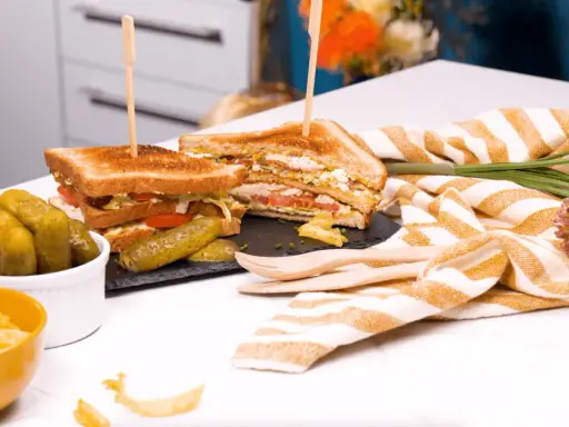 Un délicieux club sandwich, garni de tomates et de laitue, servi avec des cornichons et des chips.