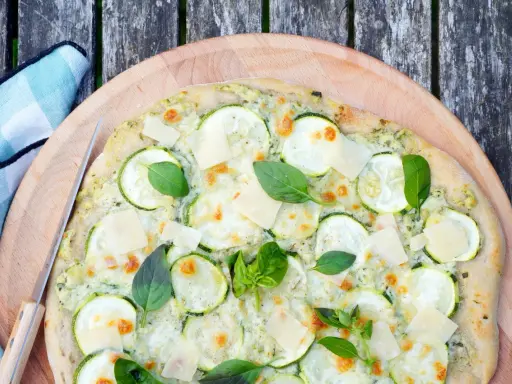 Délicieuse pizza courgette, garnie de fromage fondant, de fines tranches de courgette et de feuilles de basilic frais, prête à être dégustée.