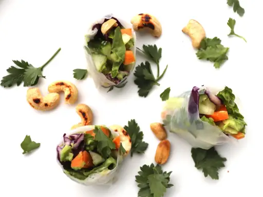 Trois rouleaux de printemps végétariens colorés, remplis de légumes frais et de noix de cajou grillées, parsemés de persil frais.