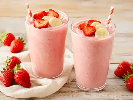 Deux verres de smoothie fraise banane, garnis de fruits frais. Parfait pour une pause gourmande et rafraîchissante.