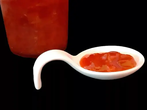 Une cuillère blanche présente une délicieuse confiture fraise rhubarbe, avec un pot en arrière-plan.