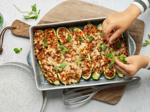 Courgettes farcies à la viande hachée, gratinées au fromage et garnies de feuilles de basilic frais. Un plat savoureux prêt à être dégusté.