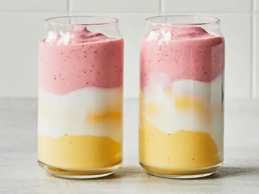 Deux verres de smoothie sans lait aux couches distinctes : jaune, blanc et rose.