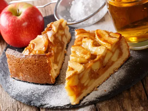 Deux parts de tarte aux pommes, saupoudrées de sucre glace, avec des pommes fraîches et un verre de cidre. Une belle idée de que faire avec des pommes.