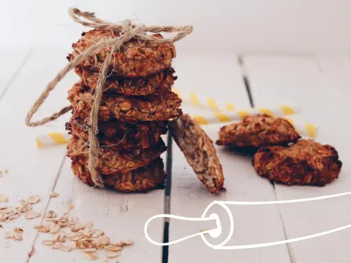 Pile de cookies healthy flocons d'avoine, liés par une cordelette. Quelques flocons éparpillés et des pailles rayées en arrière-plan.