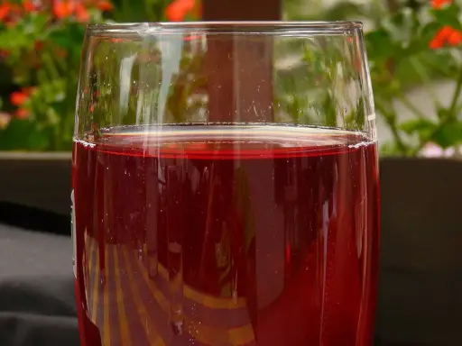 Verre de jus de raisin rouge, pétillant, avec des fleurs rouges en arrière-plan. Parfait pour faire du jus de raisin maison.